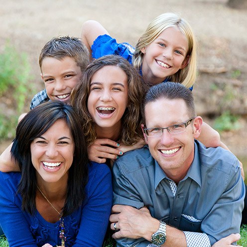 Family of five smiling while laying on their stomachs outdoors