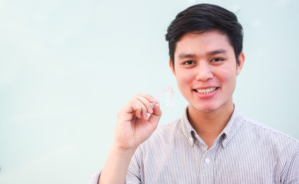 young man smiling holding Invisalign aligner