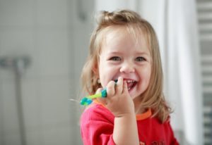 little girl in red shirt holding toothbrush 