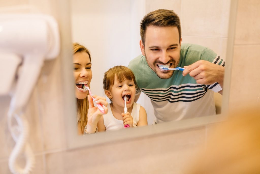 Family smiling while brushing their teeth together