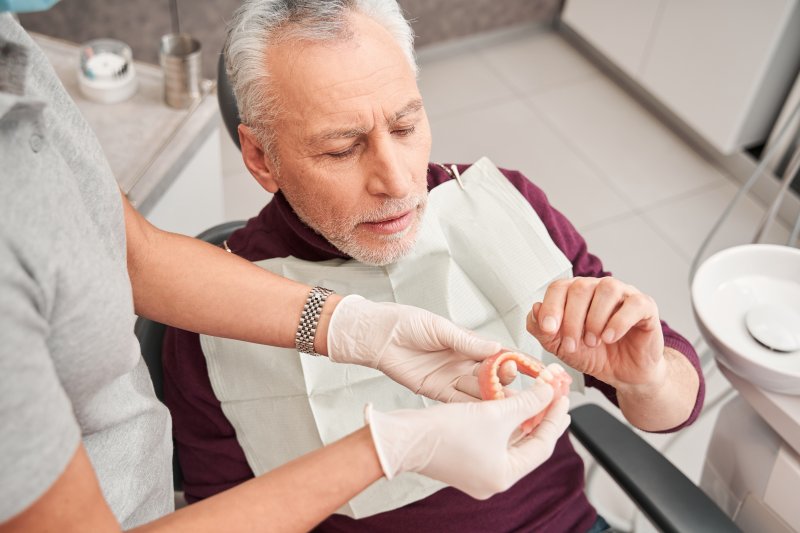 A dentist showing dentures to an older male patient